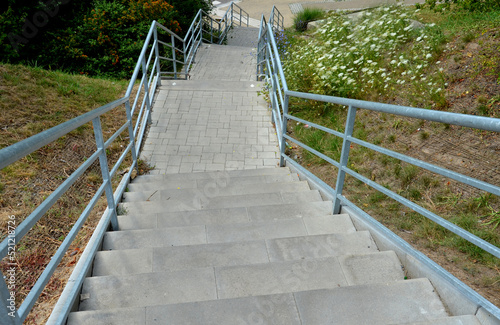 stone park long staircase with short platforms. of paved granite paving blocks. short black metal railing interrupted several times. on the upper edge there is gutter for drainage with metallic grid