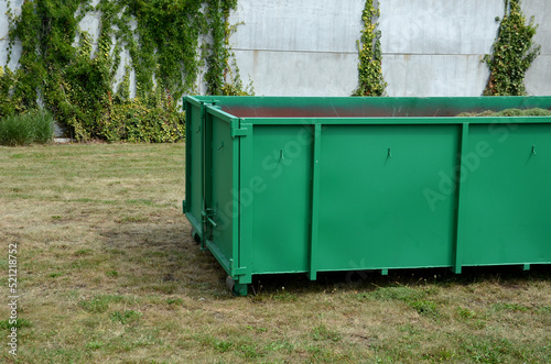 on the lawn is a green tin container for grass clippings from gardens and parks. a man checks the quality and quantity of grass by hand. a handful of green biological matter in the recycling compost