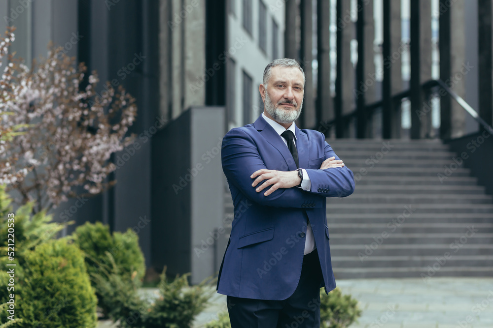 Portrait of successful director and business owner, man with crossed arms smiling outside office building, businessman investor in business suit confident