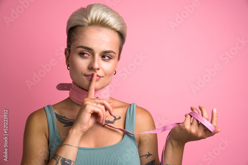 Playful woman wearing pink collar showing silence gesture over pink background photo