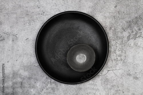 Plato redondo negro vacío y un cuenco negro sobre un fondo de mármol gris con textura. Vista superior y de cerca. Copy space