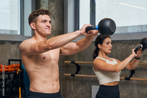 Serious male and female holding hard kettlebell during physical exercise in fitness center