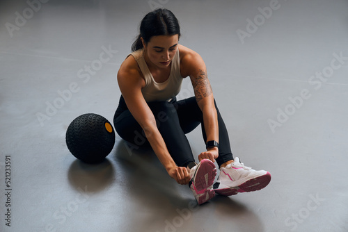 Focused female person correcting her shoes while preparing to the hard training photo