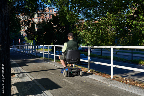 an older man rides on the bike path in an electric stroller next to a white metal fence of tubular structure