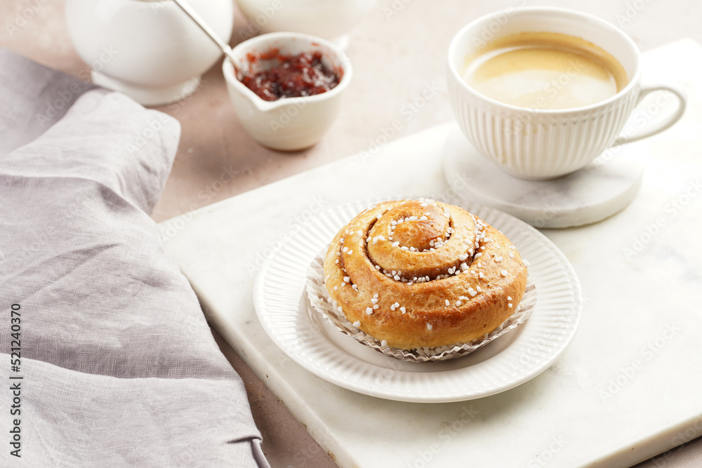 A round cinnamon pastry on a white plate on marble board, cup of coffee, jam, milk A round cinnamon pastry on a white plate on marble board, cup of coffee, jam, milk