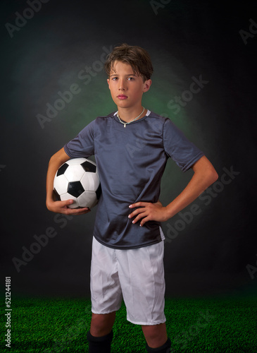 Child posing in the foreground on a black background, with a classic white soccer ball with black pentagon shaped inserts. © trattieritratti