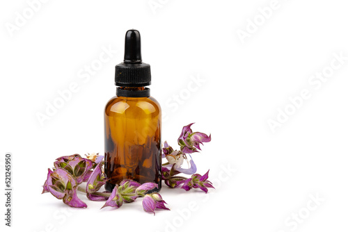 A bottle of essential oil with fresh blooming clary sage twigs on white background.
