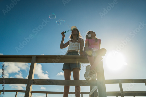 Schilderij op canvas Positive children wearing bright clothes blowing soap bubbles at the open air