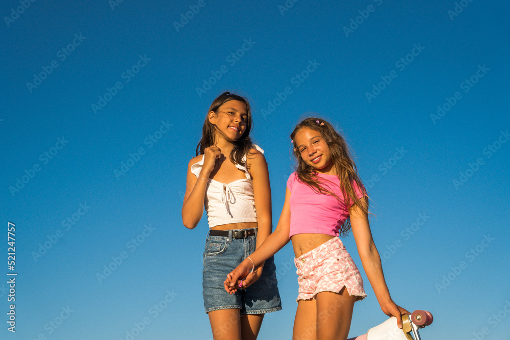 Kid girls smiling toothy while posing to the camera with blue sky at the background Kid girls smiling toothy while posing to the camera with blue sky at the background