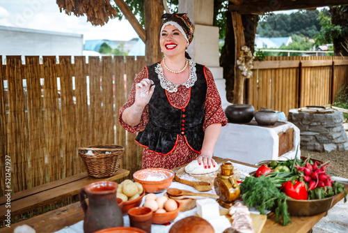 a bright cheerful Ukrainian Kuban Russian Belarusian woman in a national costume cooks traditional food in a summer kitchen in the courtyard under a canopy