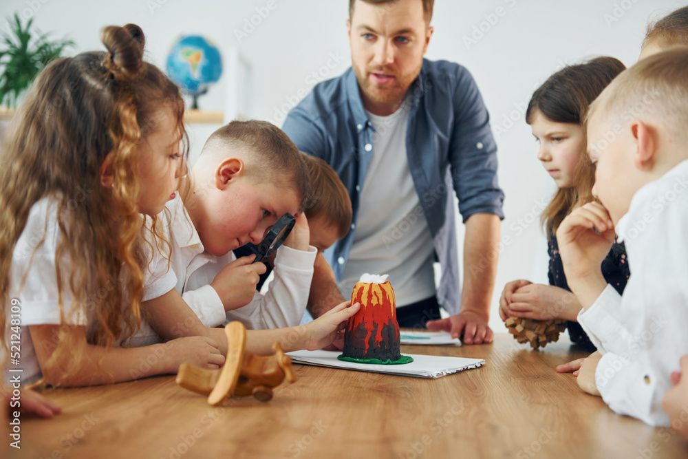 Looking at the model of volcano. Group of children students in class at school with teacher