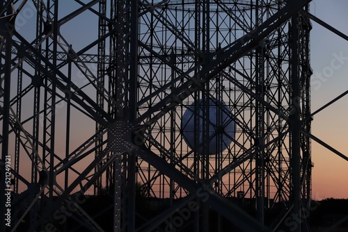 Foto Metal structure of the disused gasometer in Rome, in the center there is a large white ball that resembles the moon, in the background sky at sunset