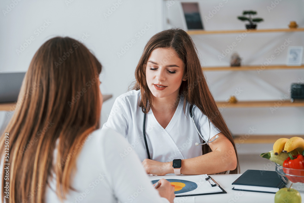 Female visitor is sitting with doctor. Professional medical worker in white coat is in the office Female visitor is sitting with doctor. Professional medical worker in white coat is in the office