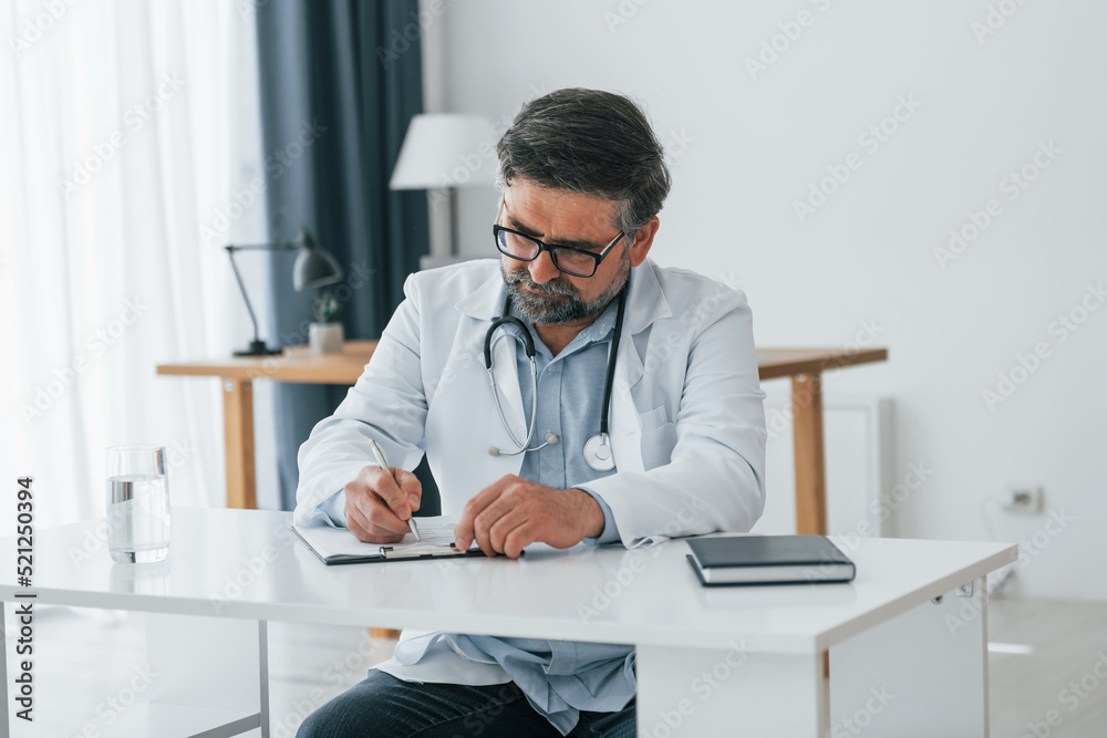 Man writing information into the document. Professional medical worker in white coat is in the office Man writing information into the document. Professional medical worker in white coat is in the office