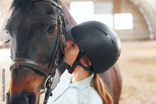 Kissing the animal. A young woman in jockey clothes is preparing for a ride with a horse on a stable © standret