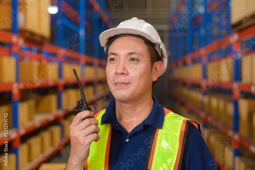 Young asian male worker wearing helmet using talki walki in modern warehouse. photo