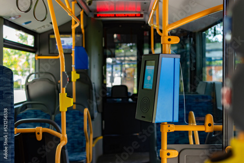 Blue contactless card or ticket validator installed on a yellow pole inside the bus with a view to the driver cockpit