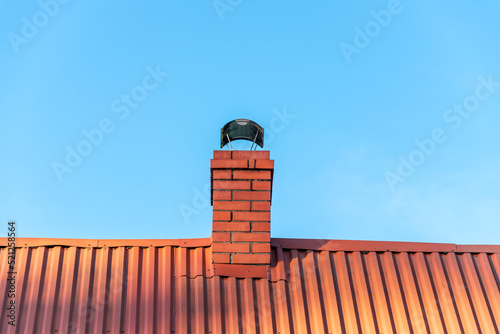 brick chimney made of clinker bricks with a chimney cowl. The roof is covered with corrugated steel in red. Blue sky in the background