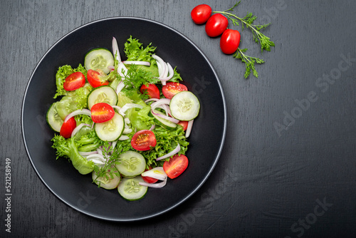 Healthy vegetable salad in black bowl on wood background.