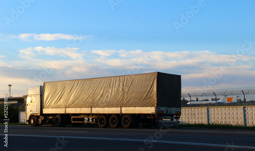 Long truck on a highway near the fence of the transport airport with planes
