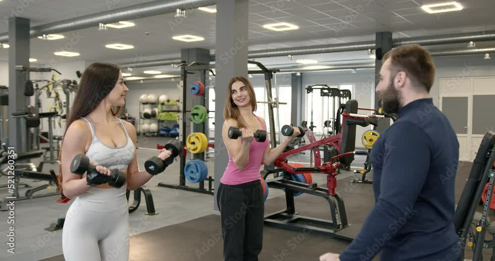 Two attractive girls in sportswear perform exercises with a coach Two attractive girls in sportswear perform exercises with a coach