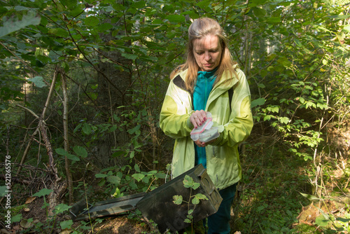 A woman in woods finds a large geocaching container.