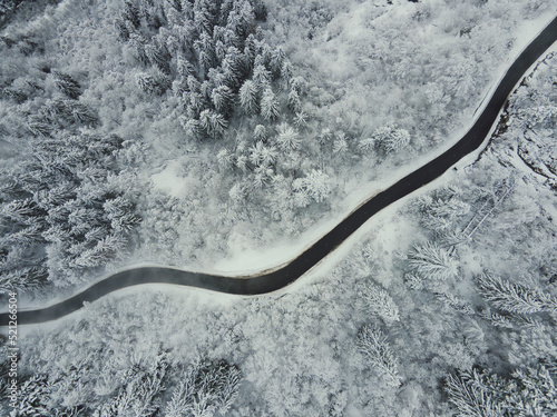 Curvy road in the winter mountains in a snowy forest. Aerial drone top-down photo of a winding mountain road in the French Alps with trees covered in snow. © Alex