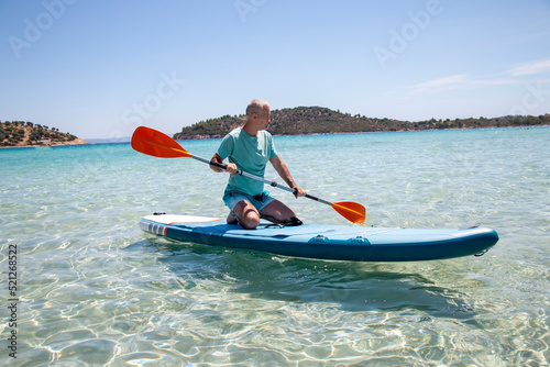 Sup surfing. Beautiful view of the sea with a mature man kneeling on a board with paddle in the water. Standup paddleboarding in summer
