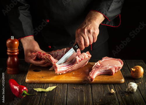 Chef or butcher cuts raw ribs on a cutting board before grilling. Meat dish idea for a hotel or restaurant