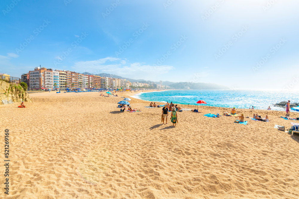 The wide sandy beach at the Costa Brava resort town of Lloret de Mar, Spain, as the fog breaks and local Spaniards and tourists enjoy the blue Mediterranean sea.