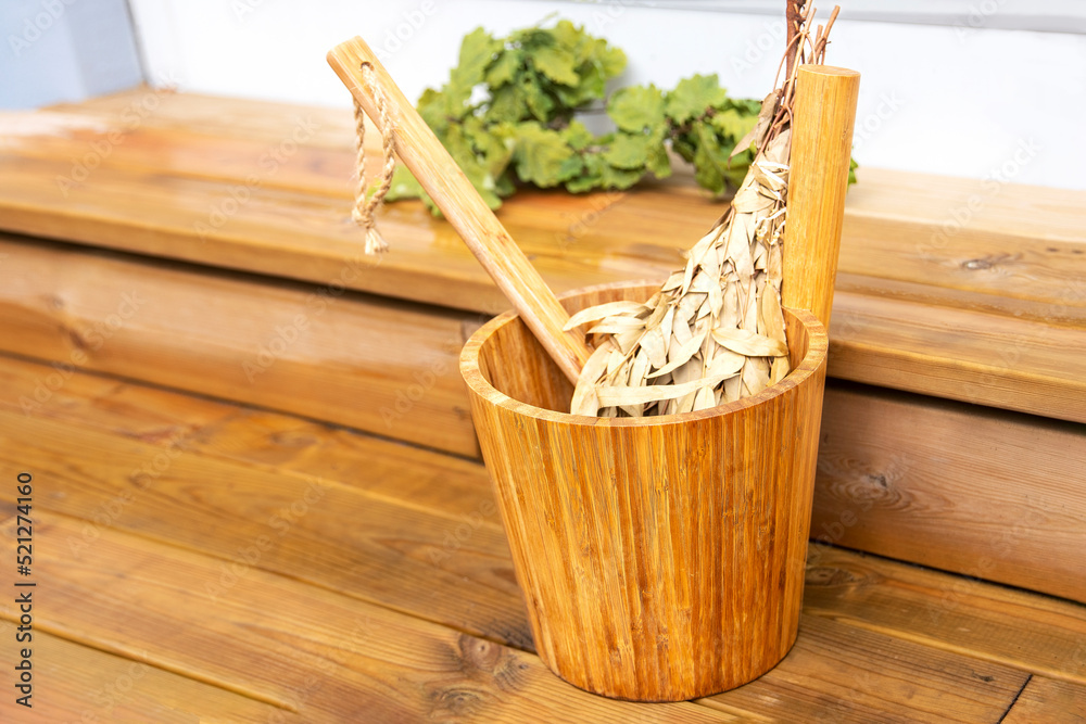 bath accessories, a wooden baul with a ladle and an odorous broom soaked in boiling water for massage, all on a wooden background and in the background a dried oak branch for aromas in the steam room
