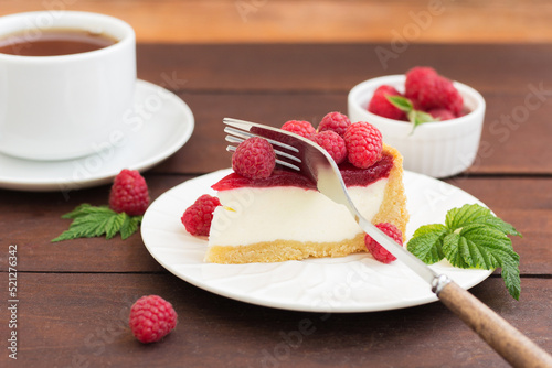 A fork cuts a piece of raspberry pie (cheesecake) lying on a plate, on a wooden background