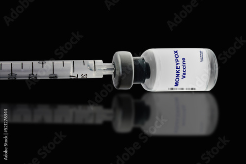 The monkeypox vaccine with a syringe close-up lies on its side against a black mirror background