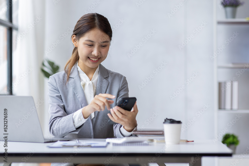 Young Asian Businesswoman uses a mobile phone and works on laptop computer in the modern home office. Young Asian Businesswoman uses a mobile phone and works on laptop computer in the modern home office.
