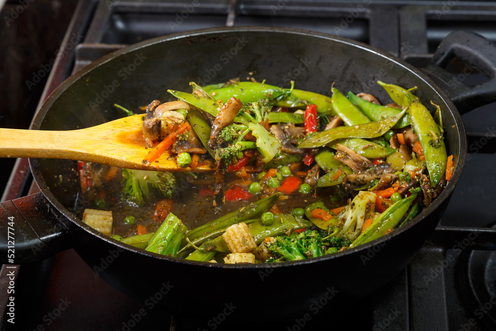 Stewed vegetables with champignon mushrooms and broccoli in a frying pan with a wooden spatula. Stewed vegetables with champignon mushrooms and broccoli in a frying pan with a wooden spatula.