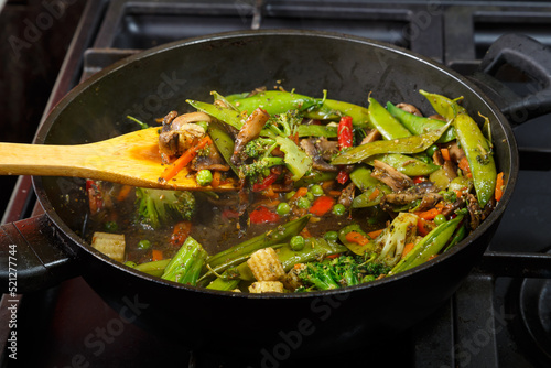 Stewed vegetables with champignon mushrooms and broccoli in a frying pan with a wooden spatula.