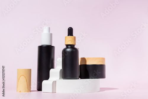 Three black glass bottles with trendy geometric shapes on a pink background.. White pedestal and ladder. Skincare products, natural cosmetic. Beauty concept for face care