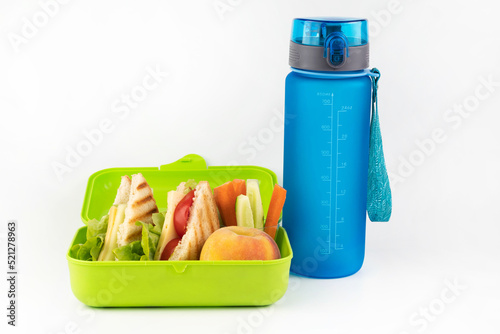 On a white background, a bottle of water, a lunch box with toasts, vegetables and peach. School snack concept.