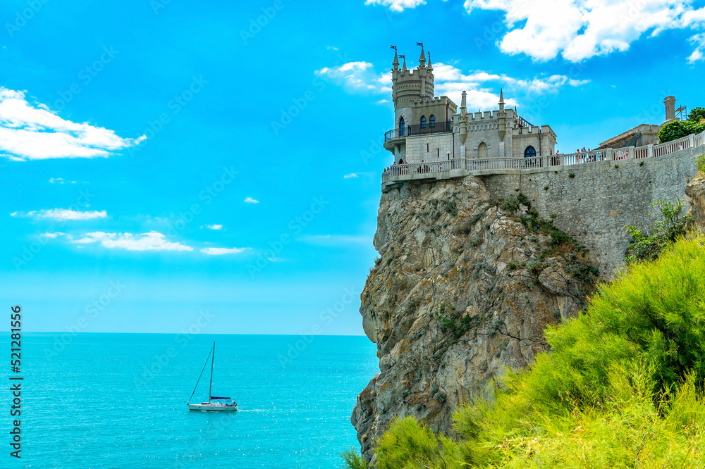 Ancient castle Swallow's Nest high on a rock near the Black Sea, Yalta, Crimea. The famous Crimean landmark - the palace at the cliff against the background of the blue sky and a white sailboat.