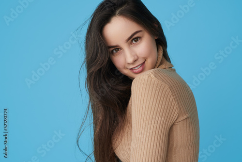 Charismatic young lady smiling at camera in blue studio