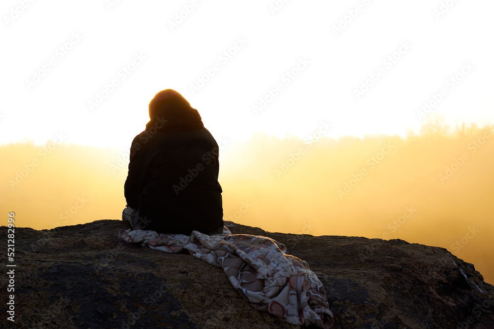 Silhouette woman sits on a rock against the backdrop of a foggy dawn