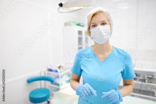 Portrait of female surgeon wearing in medical face mask and protective gloves. Doctor is preparing for surgery in operation room.