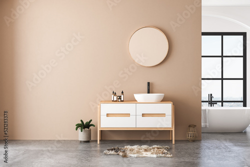 Modern bathroom interior with beige walls, white sink with oval mirror, bathtub and grey concrete floor. Minimalist beige bathroom with modern furniture. 3D rendering