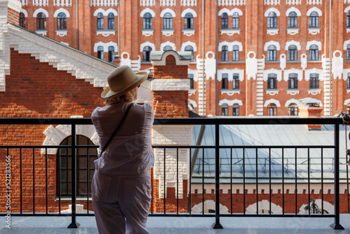 An adult stylish woman in a straw hat stands with her back against the background of beautiful buildings.