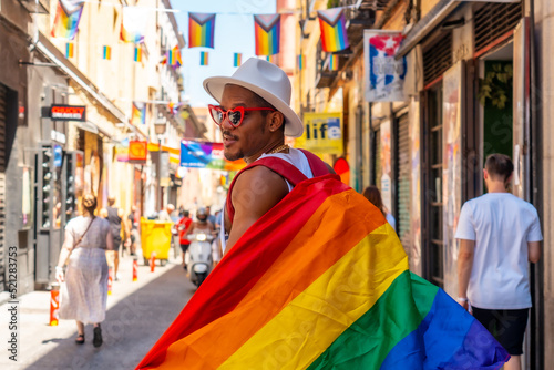 A gay black man walking at the pride party with an LGBT flag, walking backwards © unai