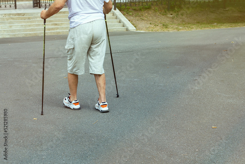 Nordic walking. An elderly man walks with sticks on the asphalt in the city