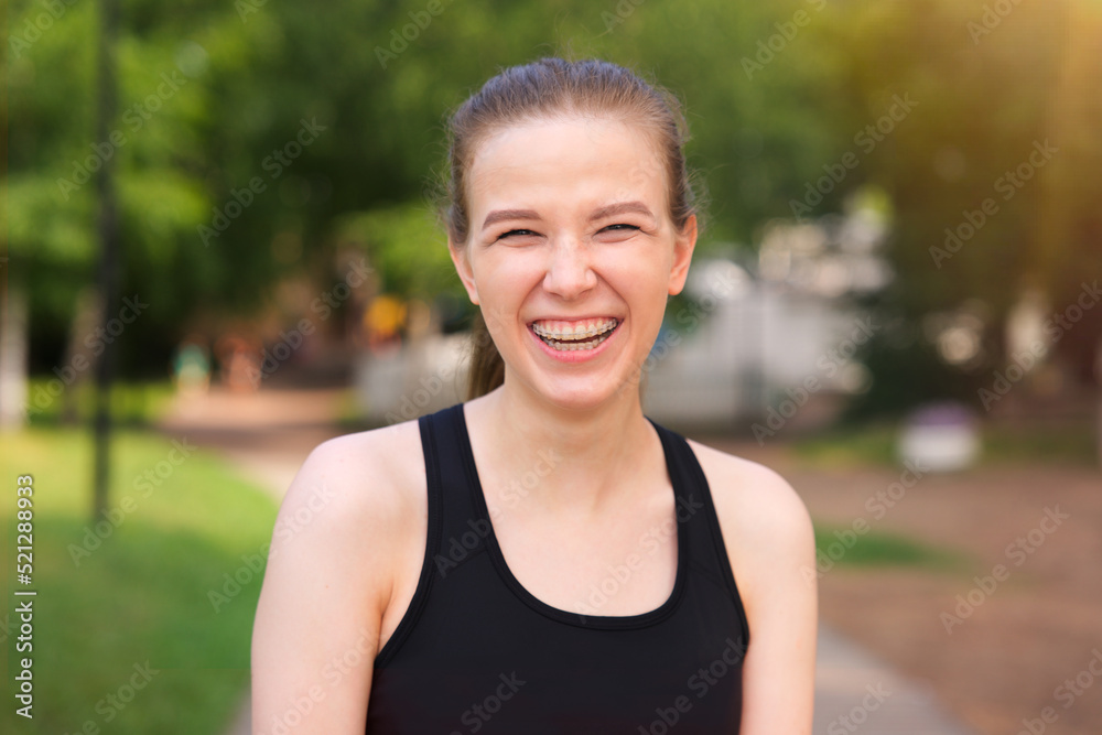 portrait of happy positive cheerful girl in braces, young beautiful excited teen teenager woman in sunglasses outdoors in summer park smiling. Runner is running, jogging, training looking at camera