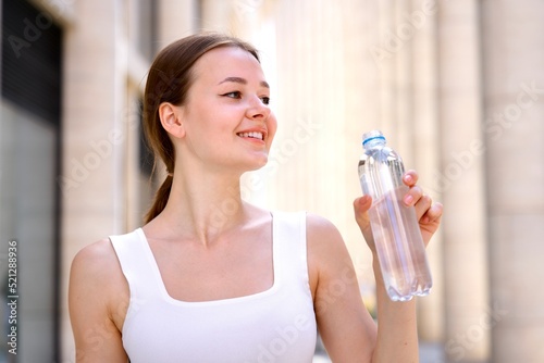 Portrait of beautiful teenager pretty girl, young happy thirsty woman is drinking pure fresh water from bottle at warm sunny summer day outdoors smiling