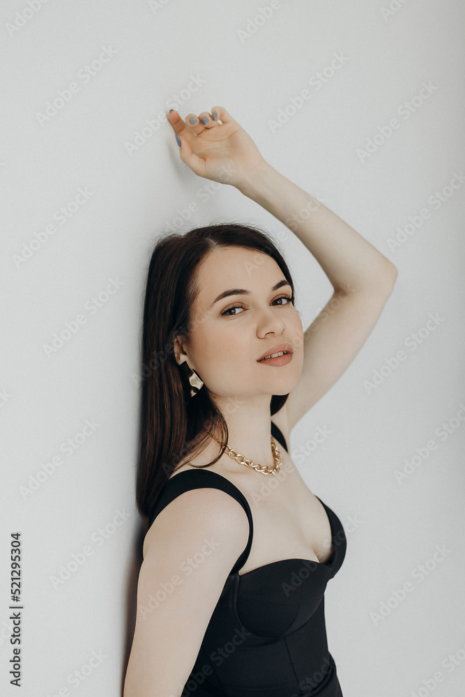 Fototapeta premium A girl in a black dress stands on a white background