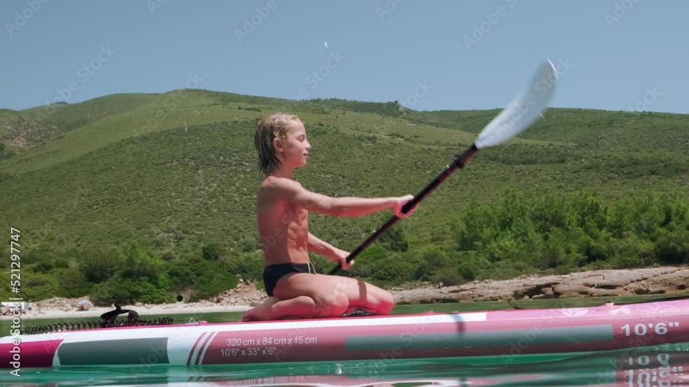 Kid paddling on paddle board in the sea, side view tracking shot, low angle.